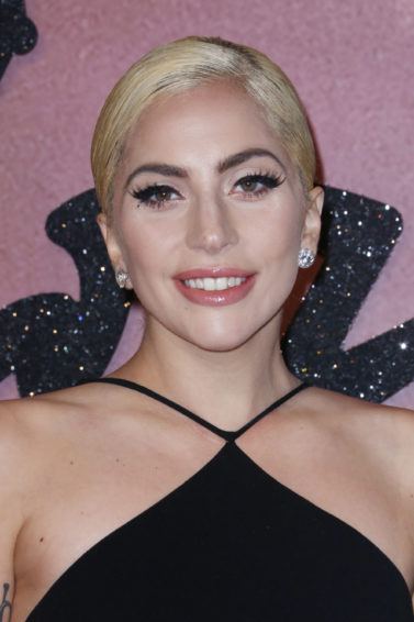 lady gaga with a sleek blonde updo, wearing black on the red carpet and posing