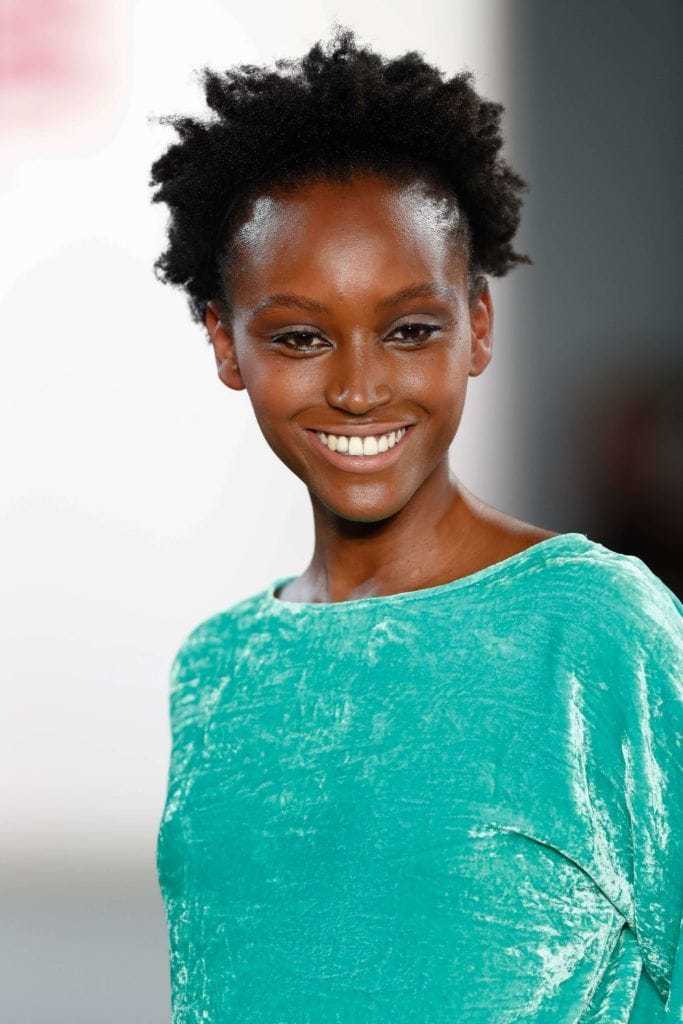 Easy hairstyles for short curly hair: Woman with natural short hair wearing a green dress on runway.