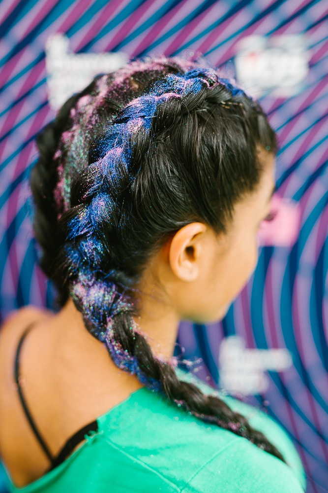 glitter coloured braids: close up shot of a woman with long boxer braids covered with glitter, wearing a teal top and posing in a festival setting