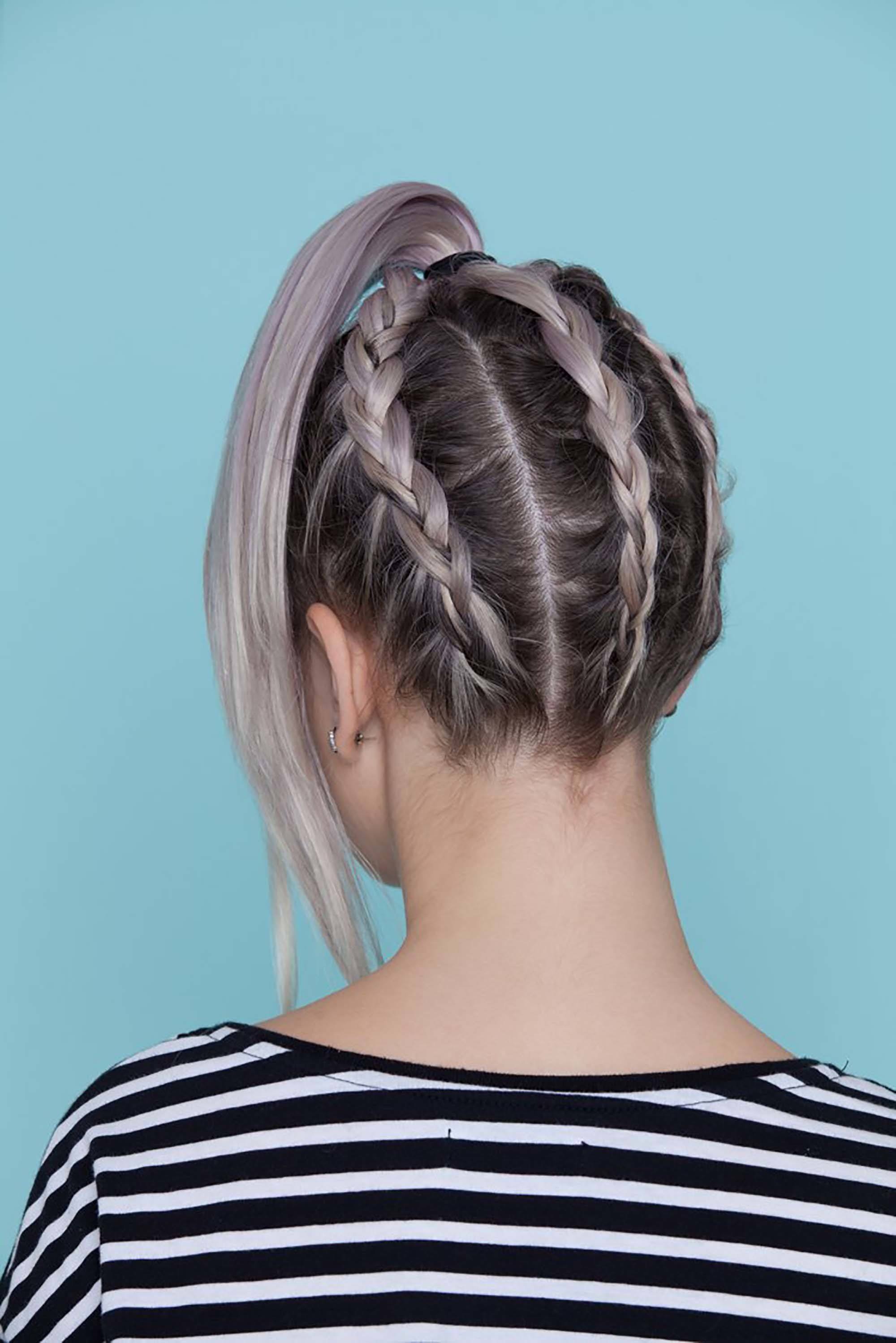 coloured braids: back shot of model with lilac hair styled into upside down French braided ponytail, wearing stripes and posing in a studio setting