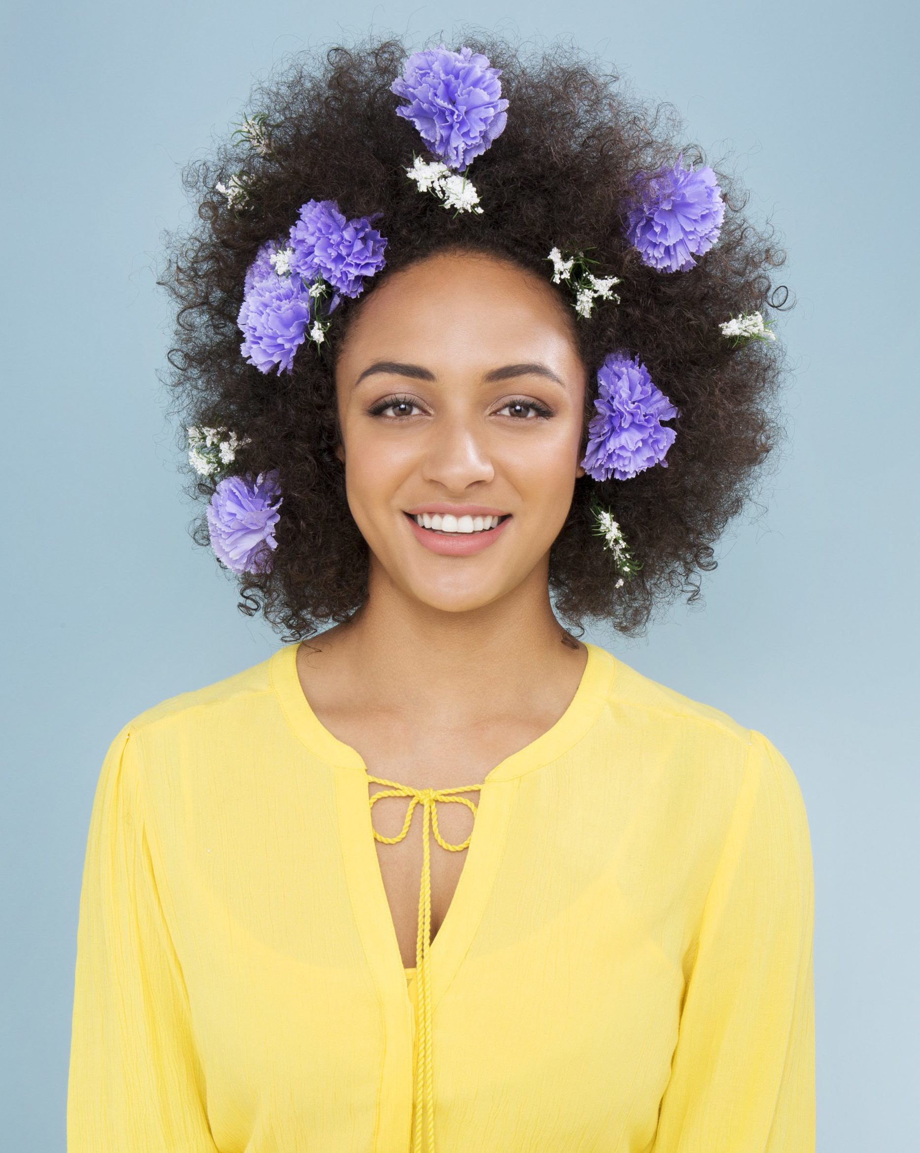 woman wearing a yellow blouse with lilac and white flower hair accessories in her afro