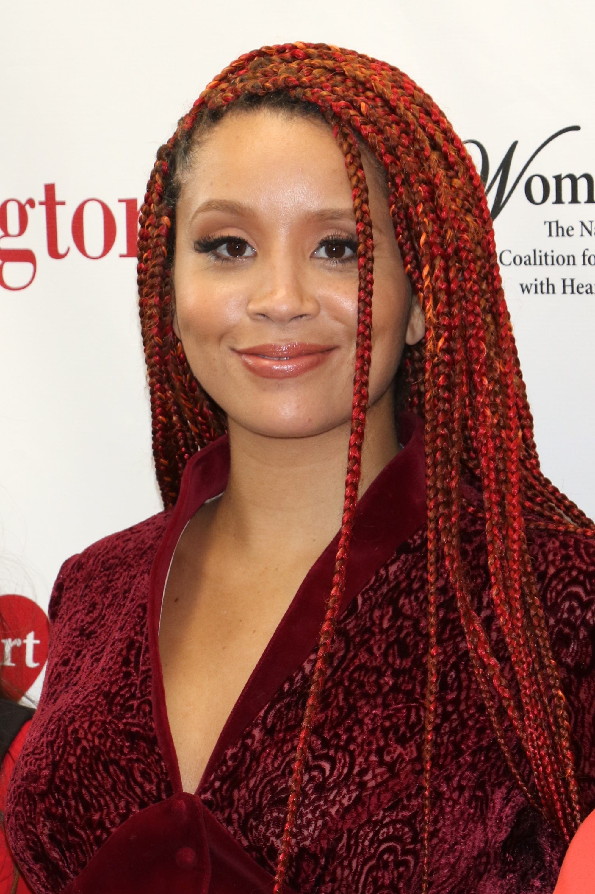 coloured braids: close up shot of jillian hervey with long red box braids, wearing a red top and posing on the red carpet