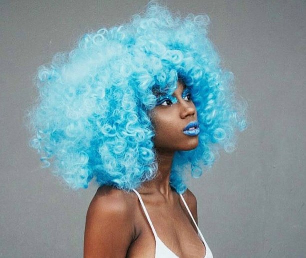 model with blue afro hair with blue makeup and white bra