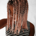 pink coloured braids: close up shot of woman with pink box braids, wearing a stripe top and posing against a white setting