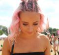 coloured braids: close up shot of a woman with medium pink wavy hair styled into half-up, half-down braided space buns, wearing a black top and posing in a festival setting