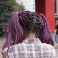 coloured box braids: close up shot of woman with purple tree braids styled into pigtails, wearing checked top and posing outside