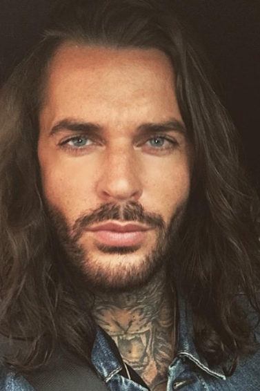 The Only Way Is Essex star Pete Wicks wearing a denim shirt with his long hair worn loose and in waves