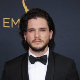 Kit Harington on the red carpet wearing a black suit with a bow tie and his dark brown hair worn long and loose with some facial hair