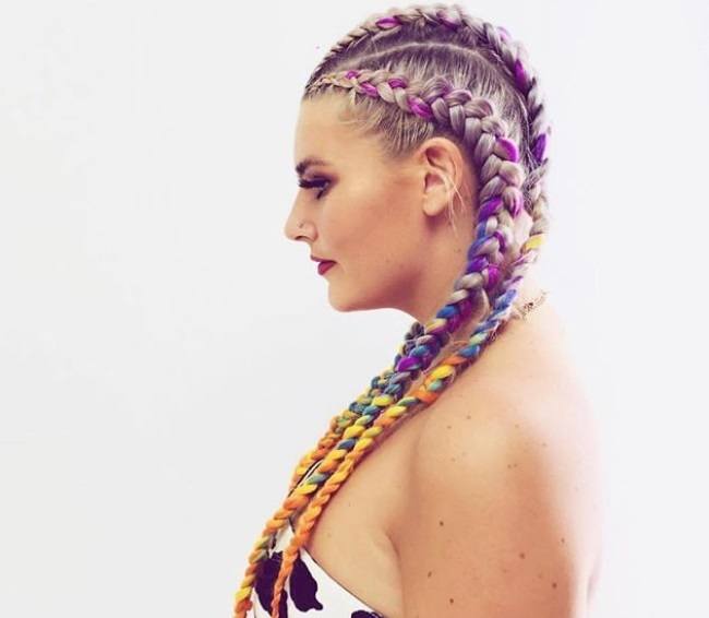 coloured braids: close up shot of a woman with straight back colourful cornrows, wearing a white bandeau top and posing in a studio setting