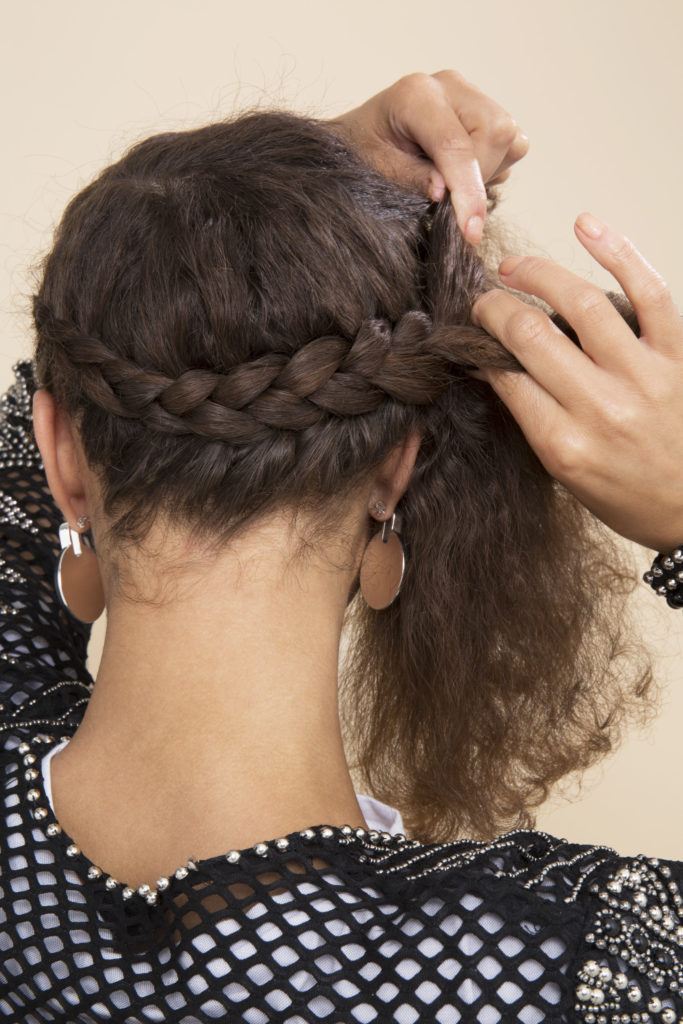 back shot of a woman with natural curly hair weaving a halo braid in the back of her head
