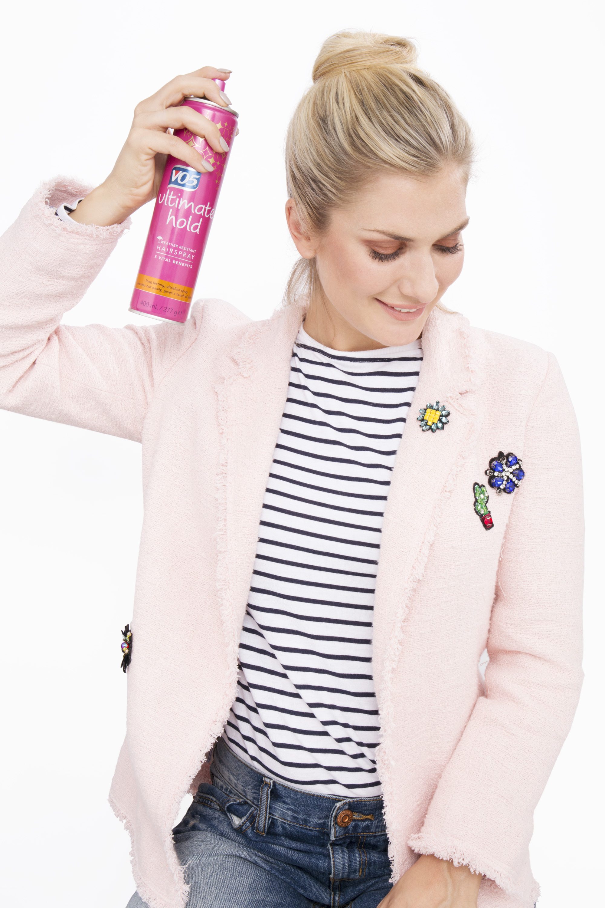 Messy bun: Woman with blonde hair with a messy high bun spraying her hair with hairspray