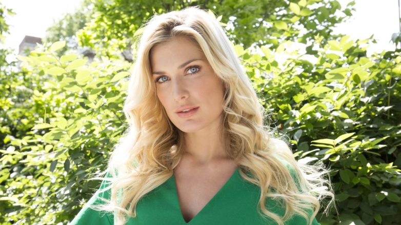 woman with long blonde hair in undone waves wearing a green dress outside