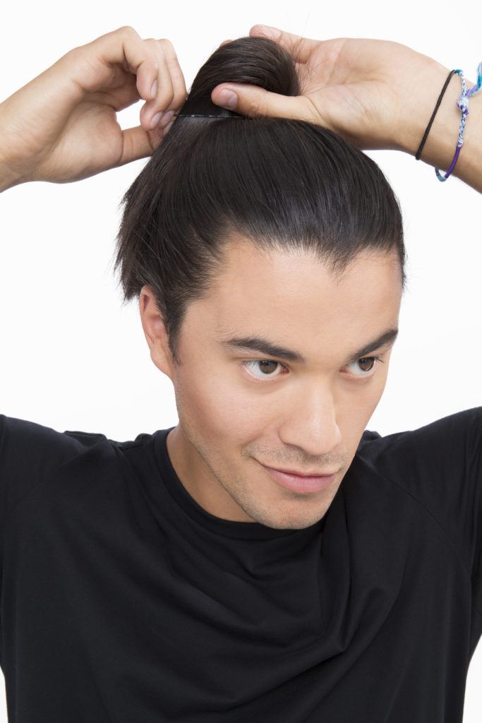 Dark haired man tying his dark brown hair