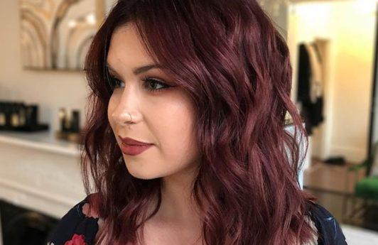 close up shot of woman with mulled wine hair colour, wearing red floral top in a salon
