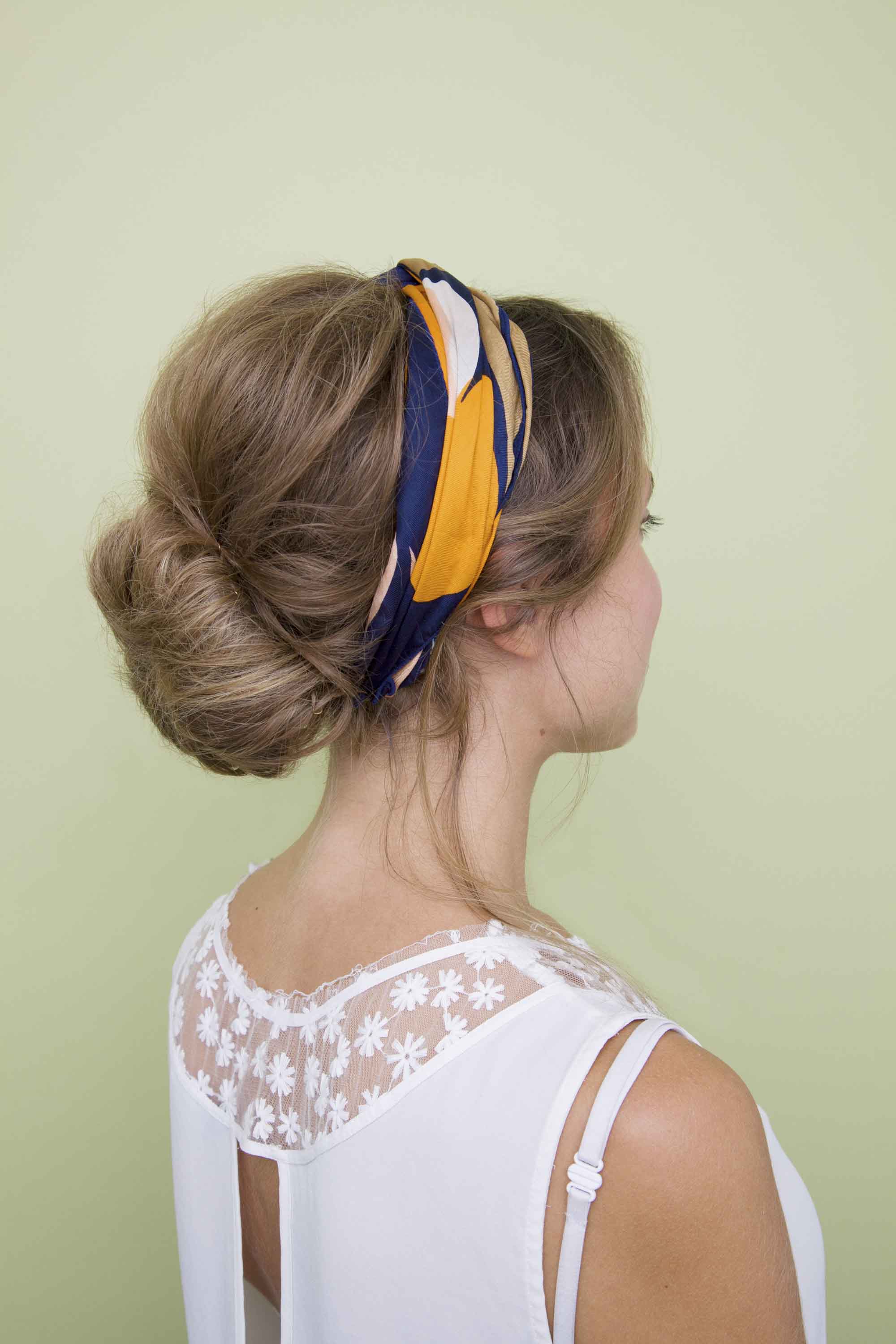 Festival hair: side view of woman with natural blonde hair styled in a low big messy bun with yellow headscarf headband in studio setting