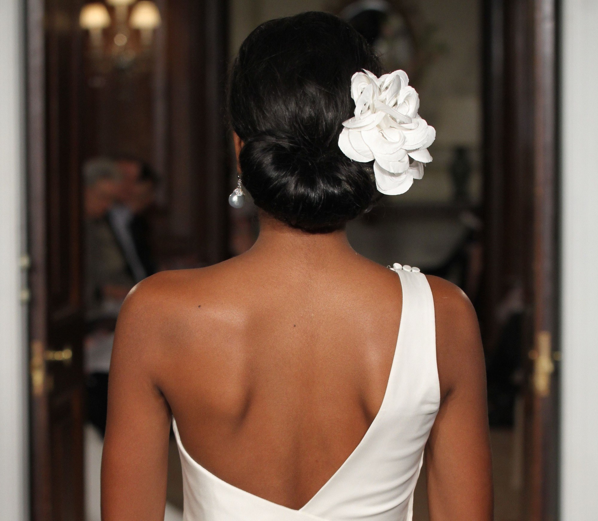 Wedding updos: Close up shot of model on the bridal runway with low rolled updo with a flower in it, wearing white open back wedding dress