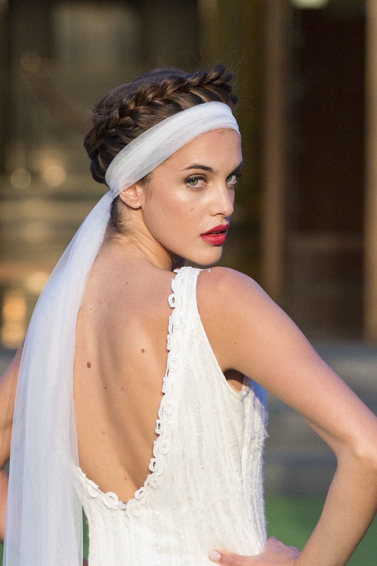 Wedding updos: Close up shot of model on the bridal runway with crown braid hairstyle, with a veil wrapped around it, wearing white dress and posing