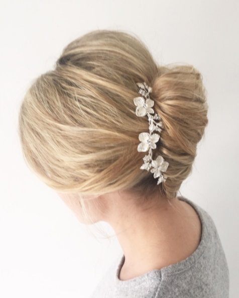 Wedding updos for long hair: Side shot of a woman with long blonde hair styled into a French twist, complete with a floral hair accessory.