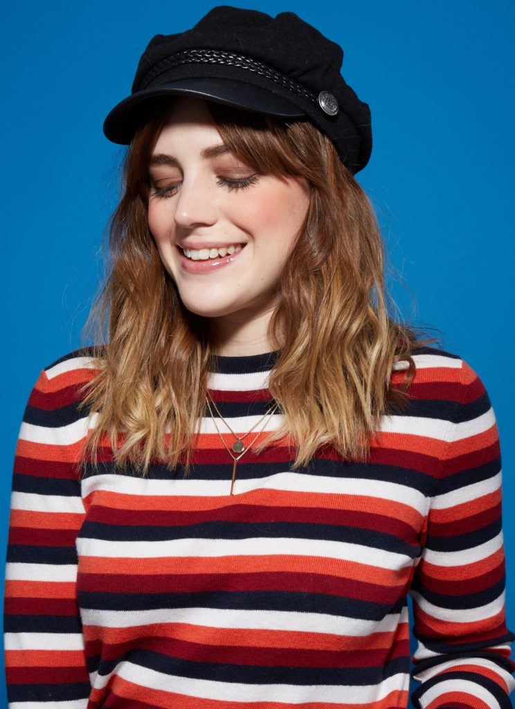 woman with medium length wavy brown hair, wearing a striped top and a baker boy hat