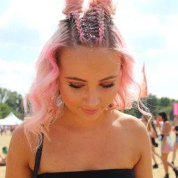 Lovebox 2018 festival hair: woman at festival with pink wavy medium length hair styled with two dutch braids down the centre going into mini buns with glitter down her roots