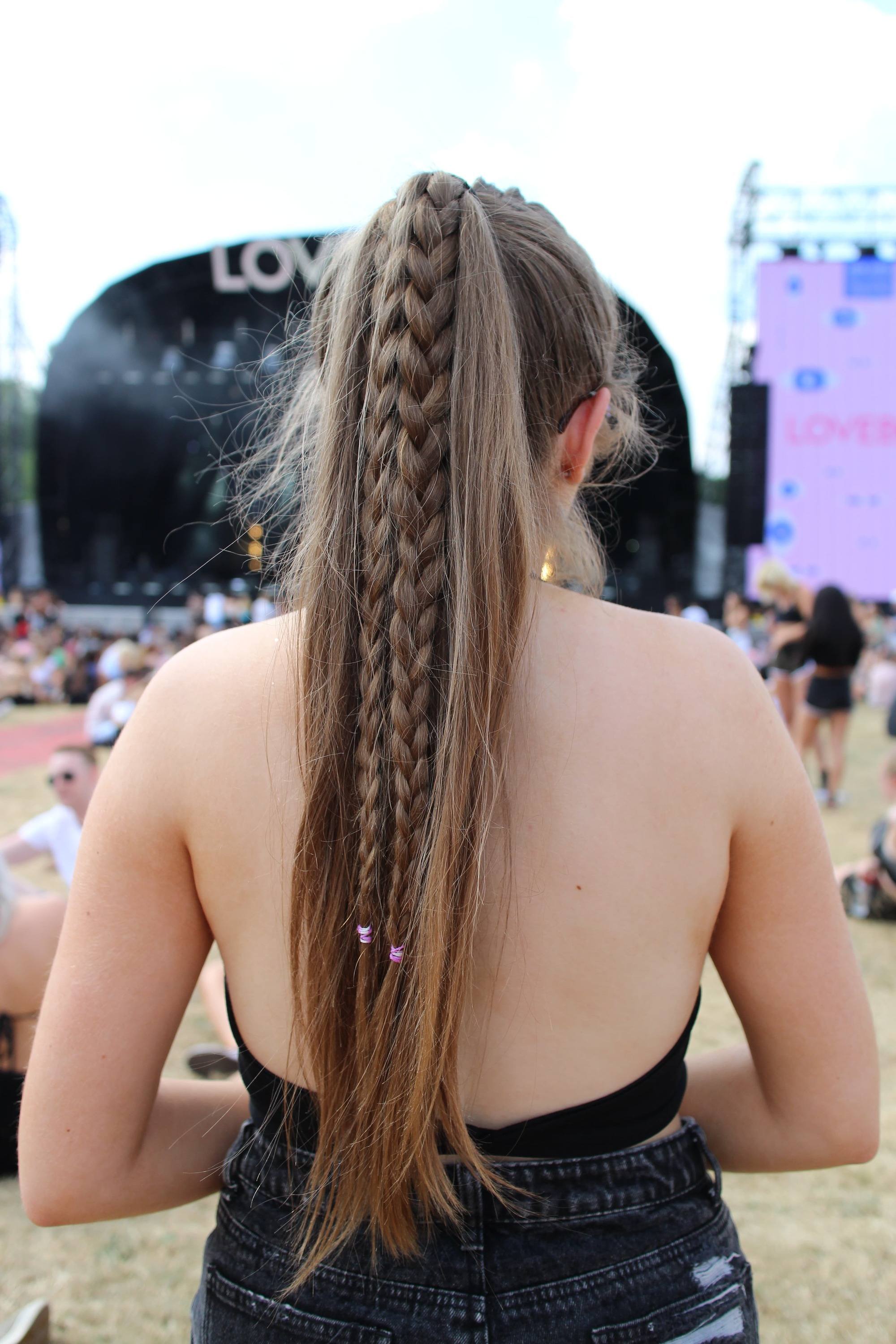 Lovebox 2018 festival hair: back view of girl with very long light brown straight hair in high ponytail with hidden braids through the length of the hair wearing a backless black top