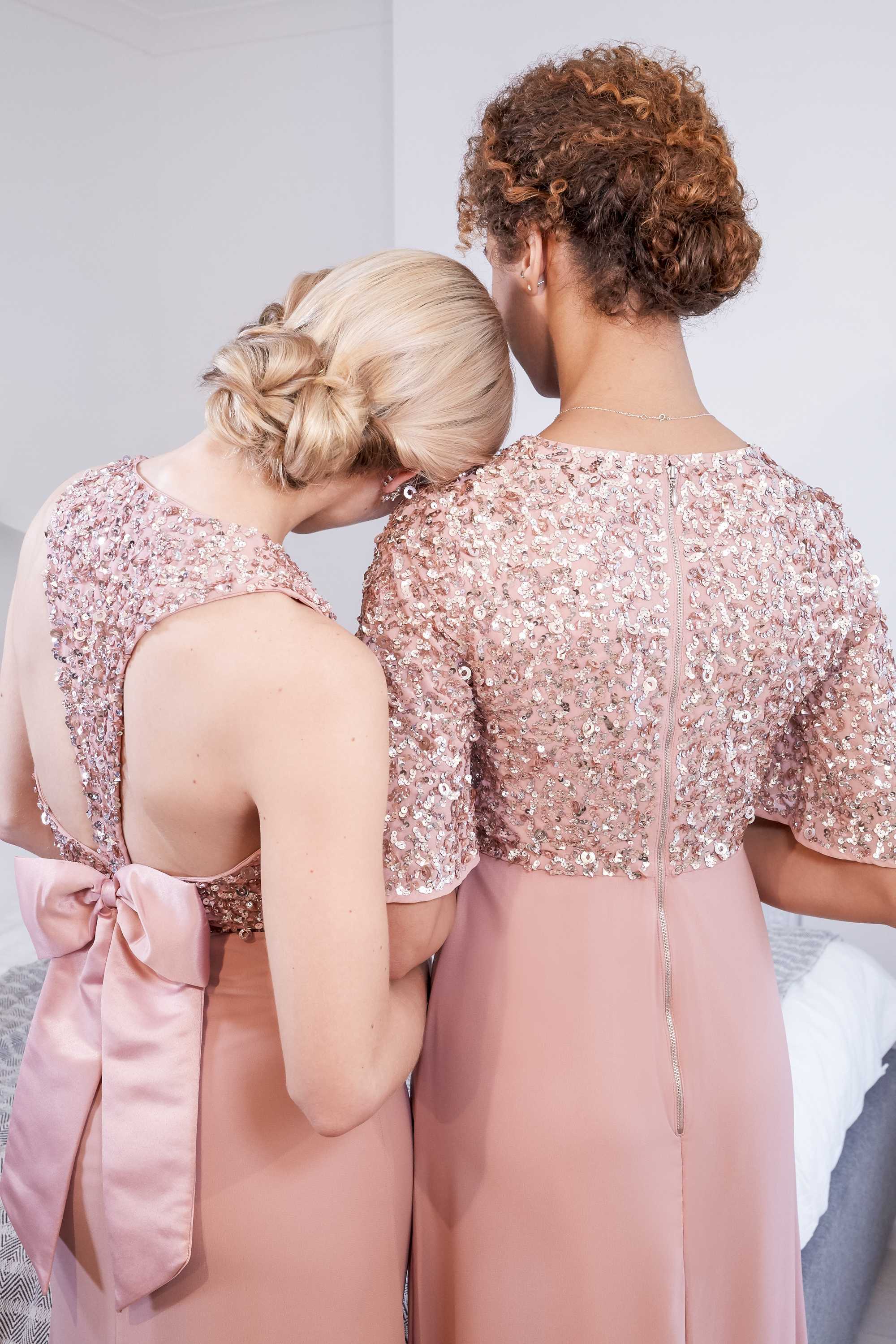 Wedding updos: Close up shot of two models with low knotted bun, wearing pink gowns and posing in a bedroom