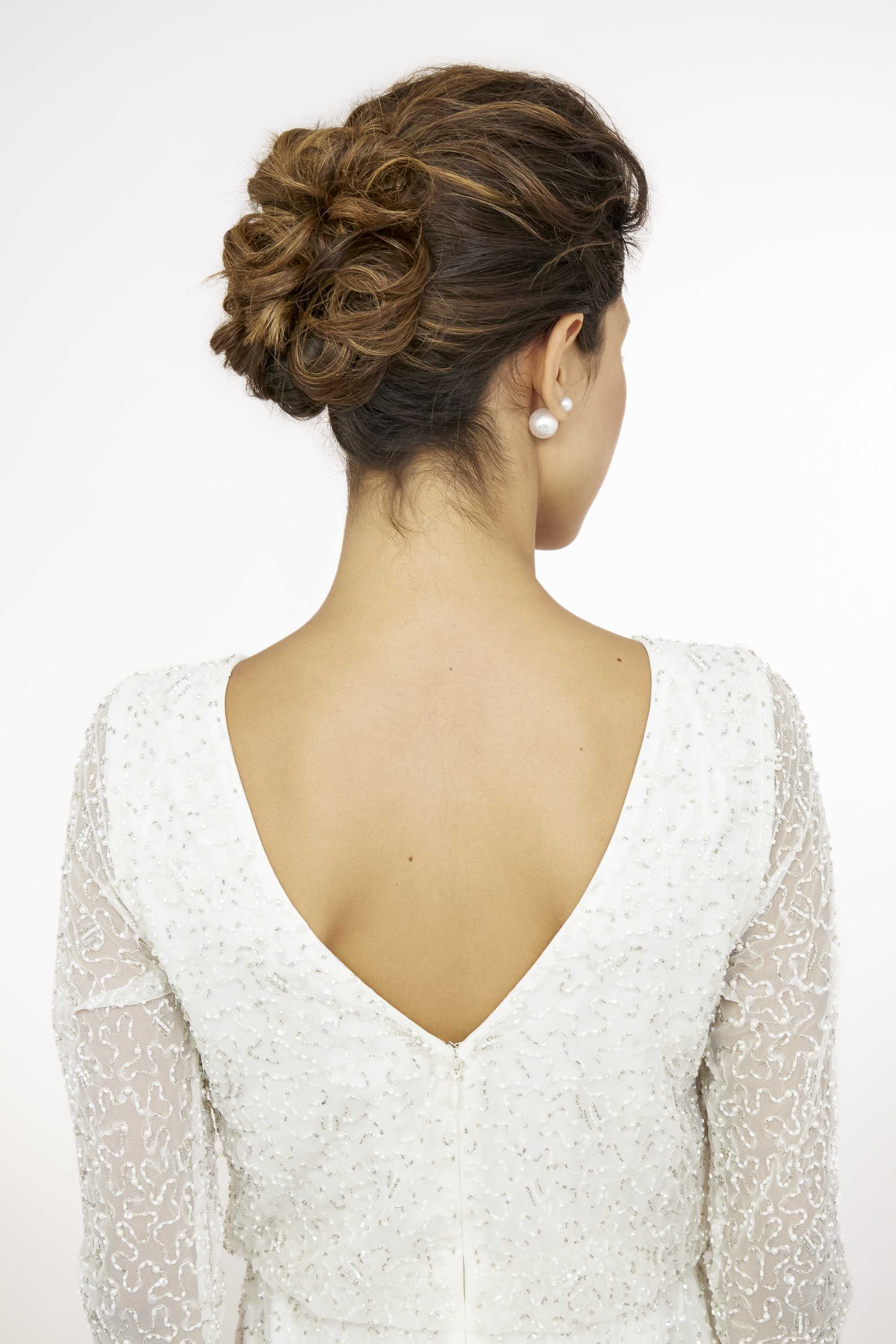 Wedding updos: Close up shot of model with wavy bridal updo, wearing white dress and posing in a studio