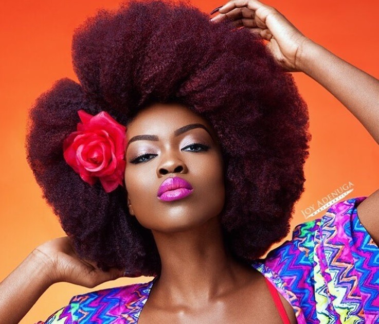 close up shot of woman with dark red afro that has been fluffed out, that has a flower in it