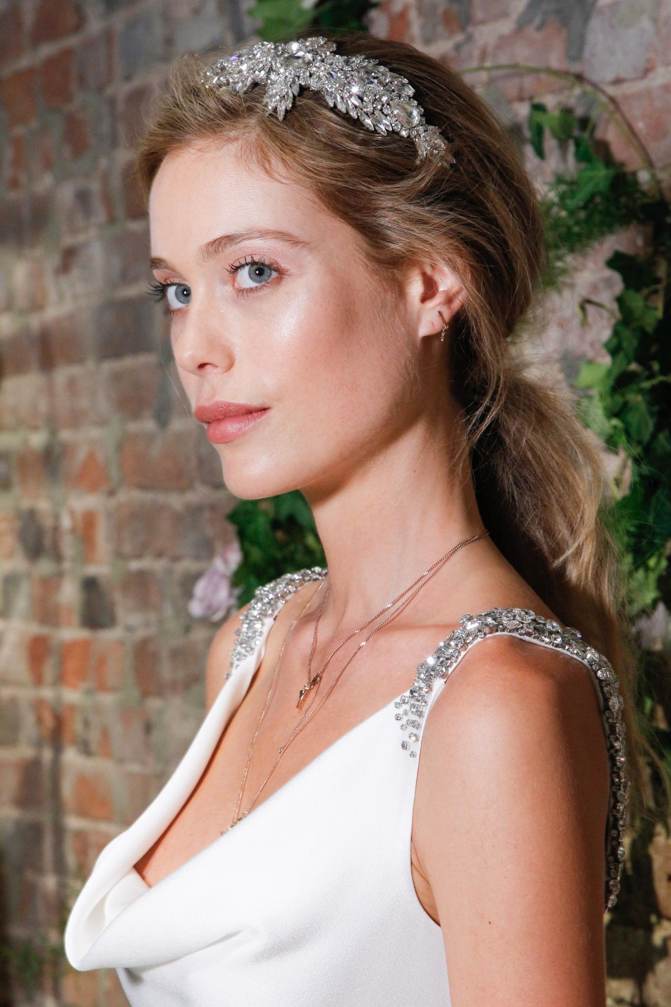 Updos for long hair: Woman with blonde hair in messy low ponytail with headband accessory wearing wedding dress