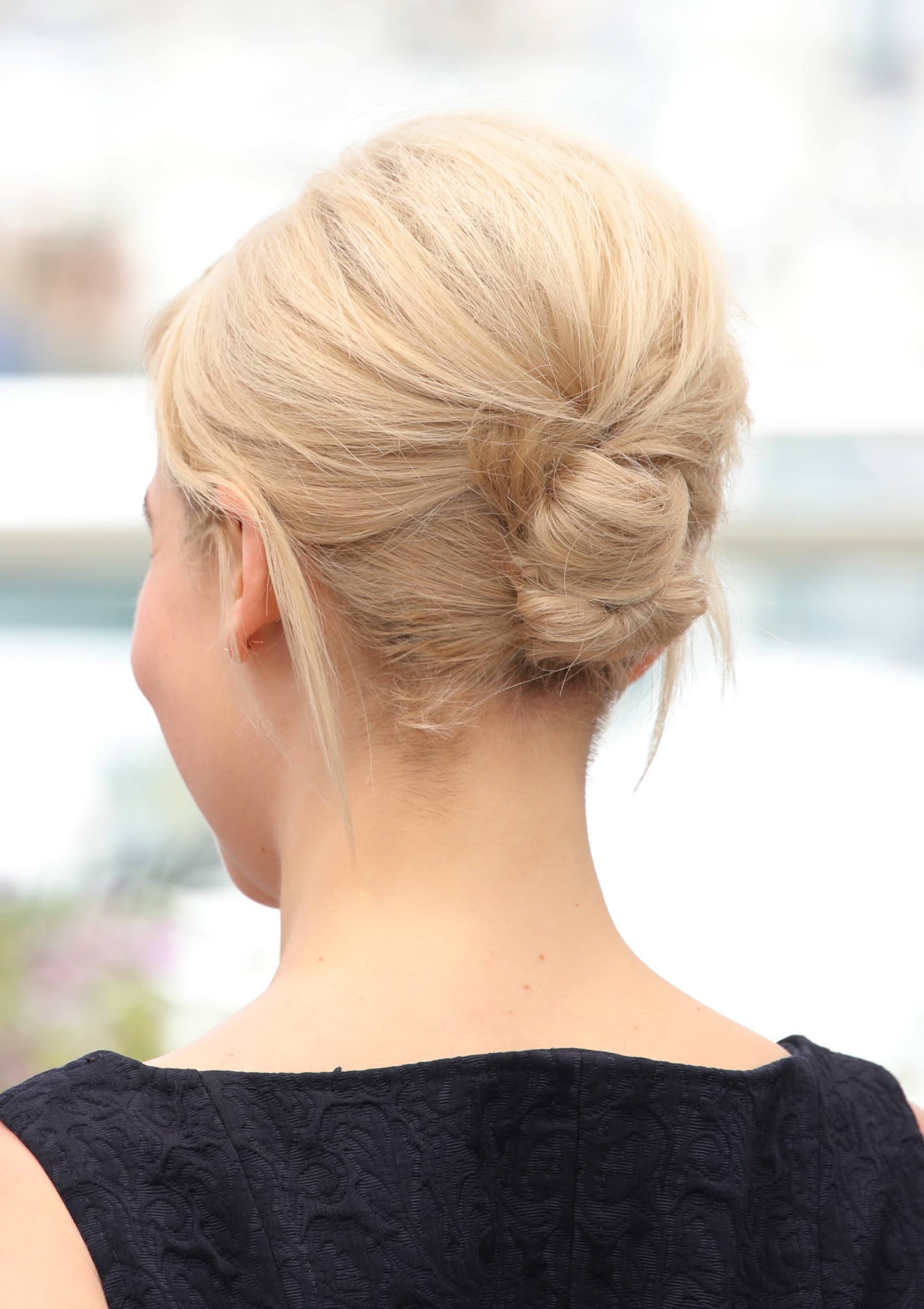 updos for medium hair: back view of emilia clarke with platinum blonde hair styled in a formal bun updo with voluminous height at the crown