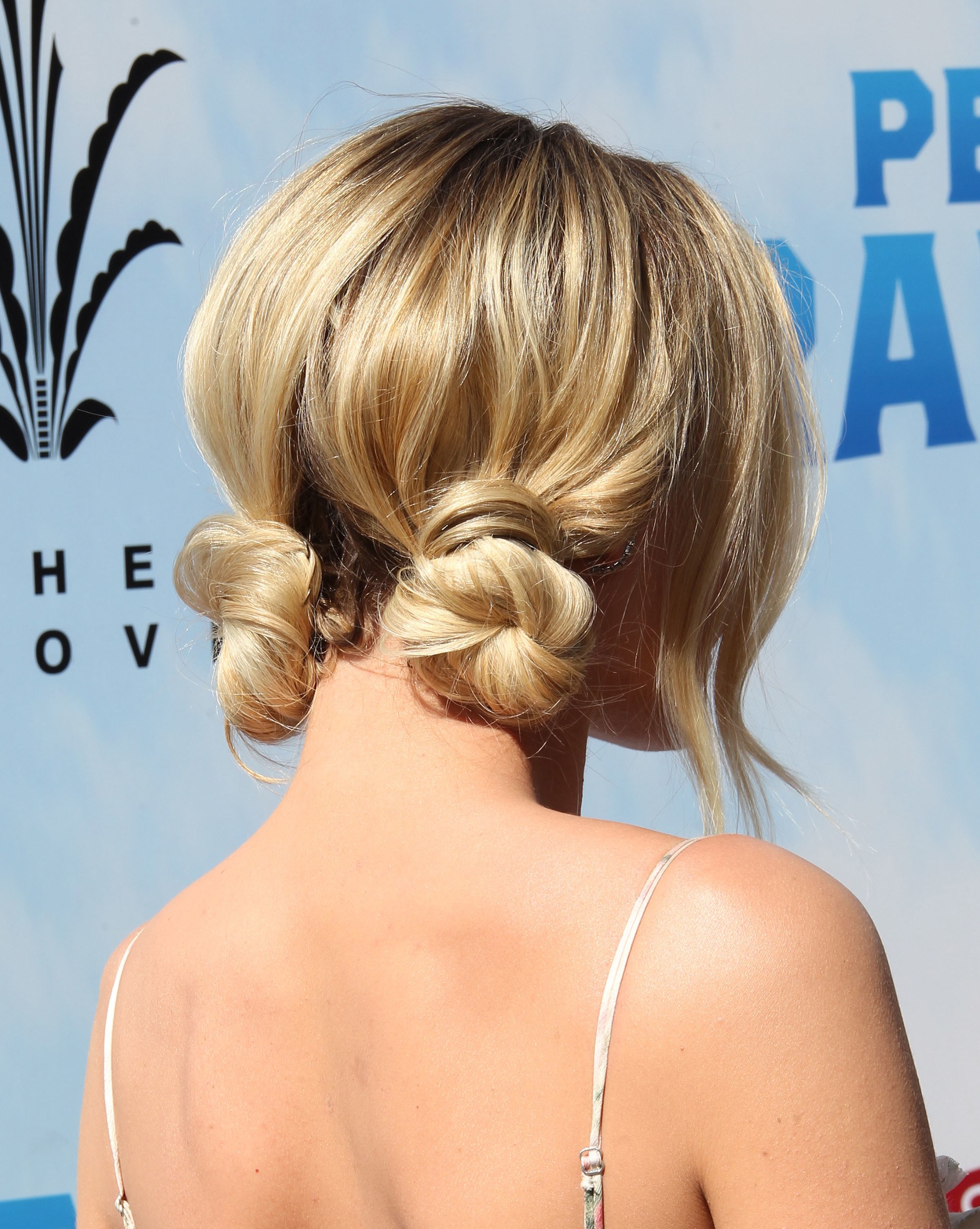 updos for medium hair: back view of margot robbie with blonde hair styled in low space buns with loose hair at the front