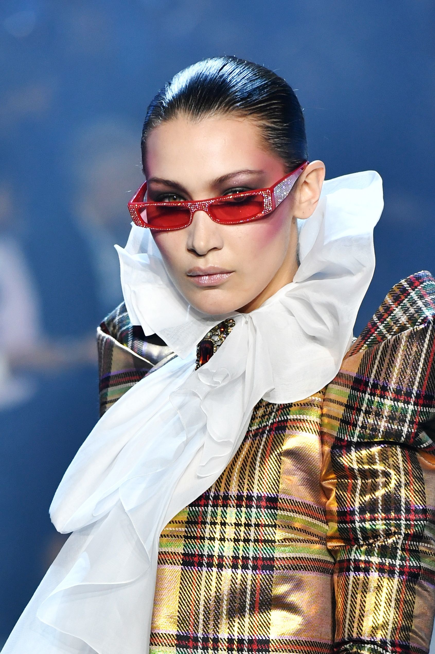 close up shot of bella hadid with micro sunglasses and slicked back hairstyle, wearing neck collar and checked shirt