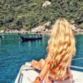 blonde woman sitting on a boat in the sea with long curly blonde beach hair