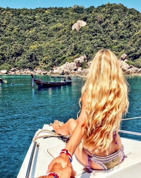 blonde woman sitting on a boat in the sea with long curly blonde beach hair