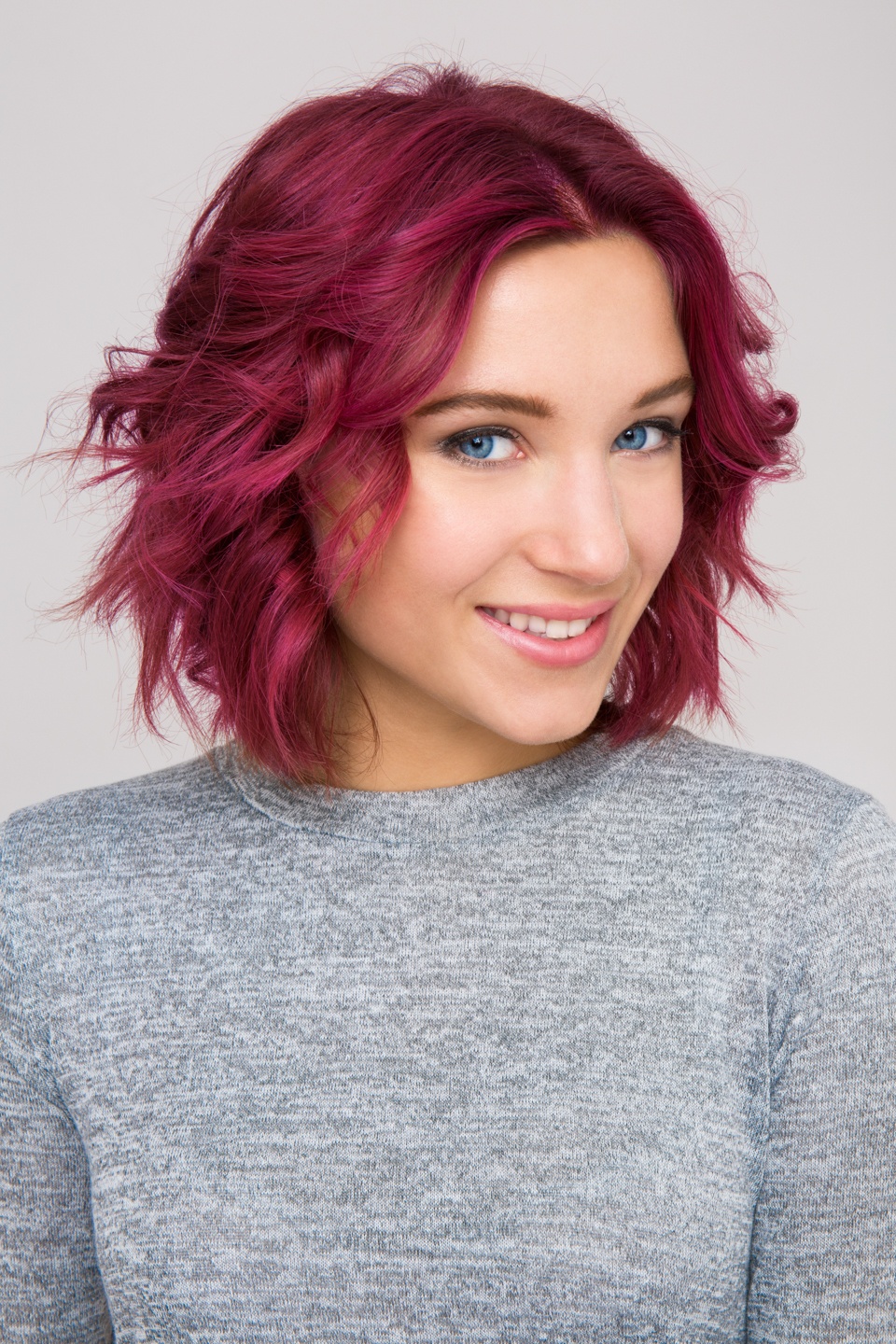 Shampoo full guide: Woman with short coloured pink red wavy hair wearing a grey jumper.