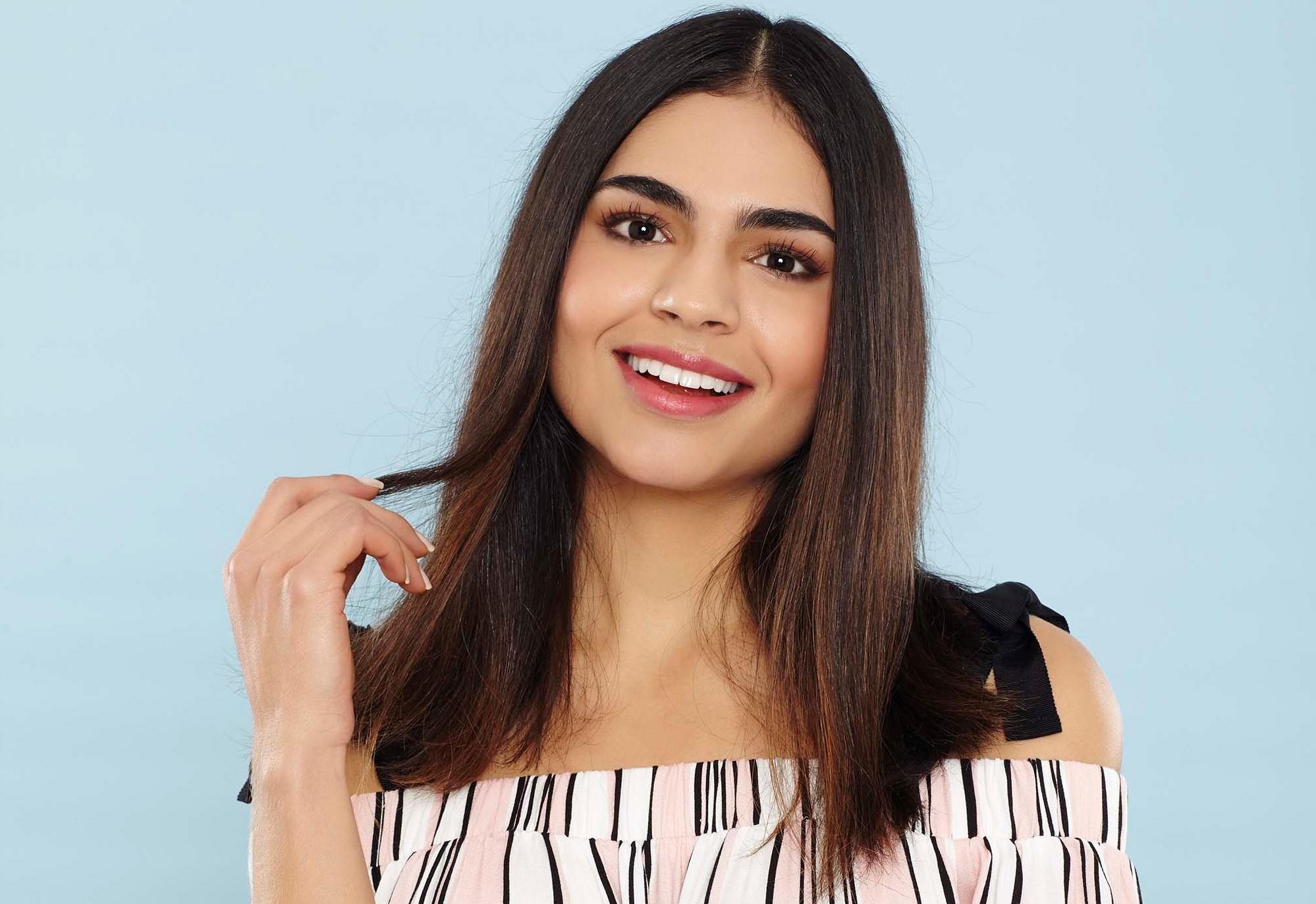 Shampoo full guide: Woman touching her medium length brown hair wearing a striped bardot off the shoulder top.