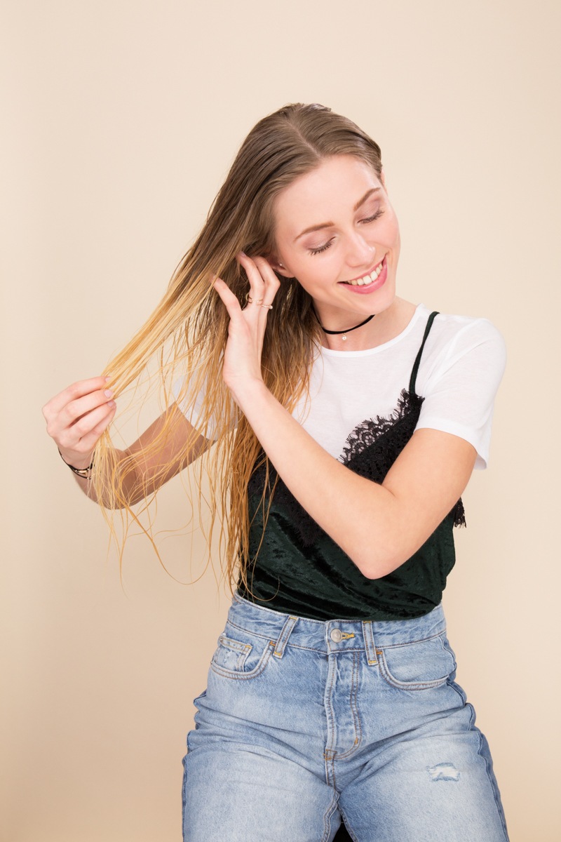 Shampoo full guide: Woman finger combing her straight long blonde hair wearing a t-shirt ad cami with jeans.