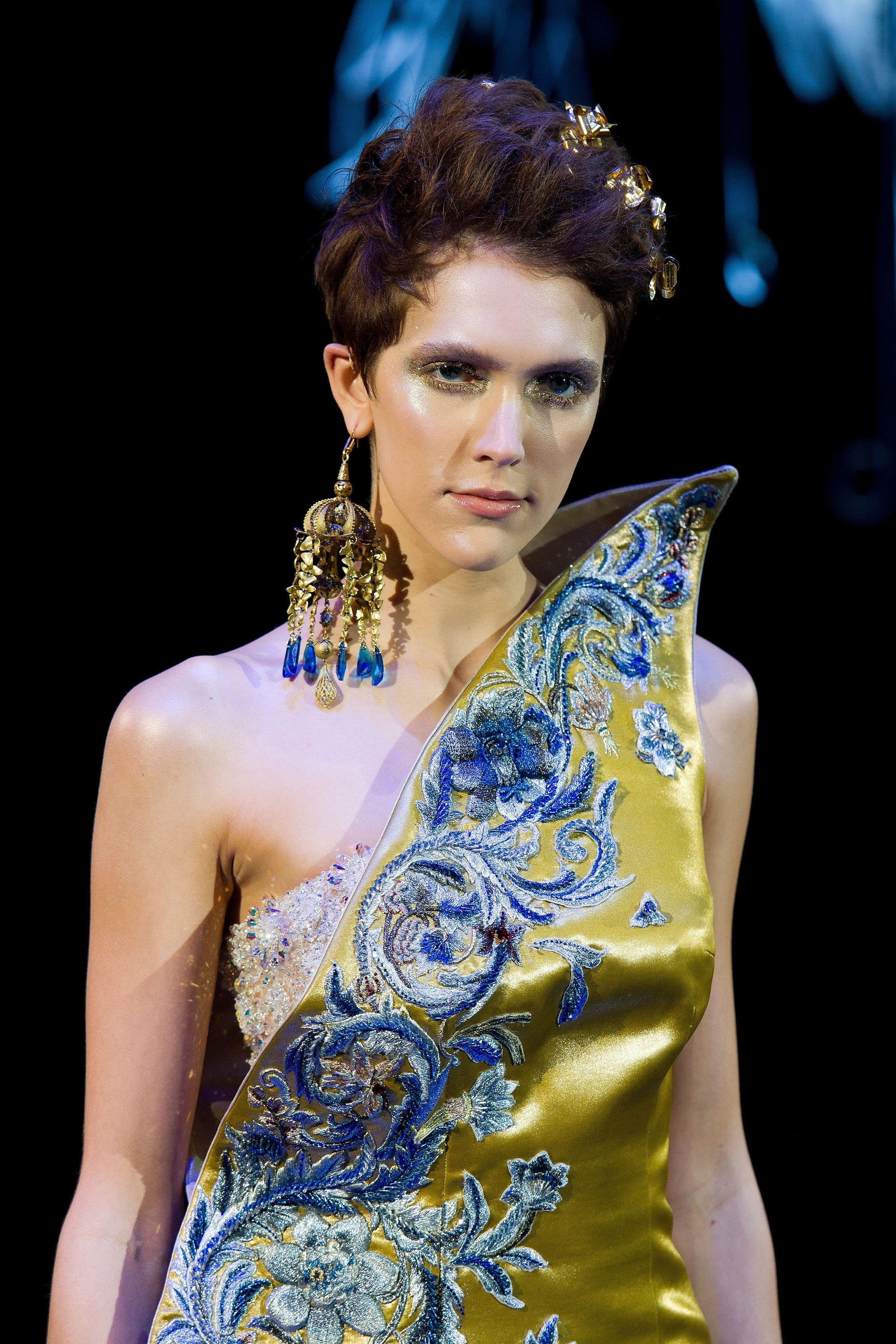 close up shot of model on the guo pei runway with golden hair accessories in her mane, wearing satin dress and statement earrings