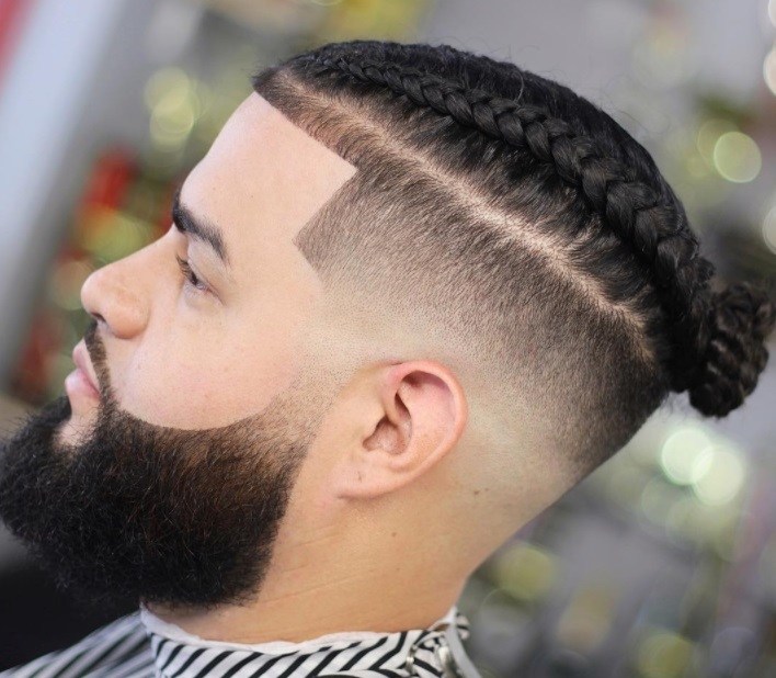 close up of a man with braided top knot men's hairstyle with undercut and beard at a salon