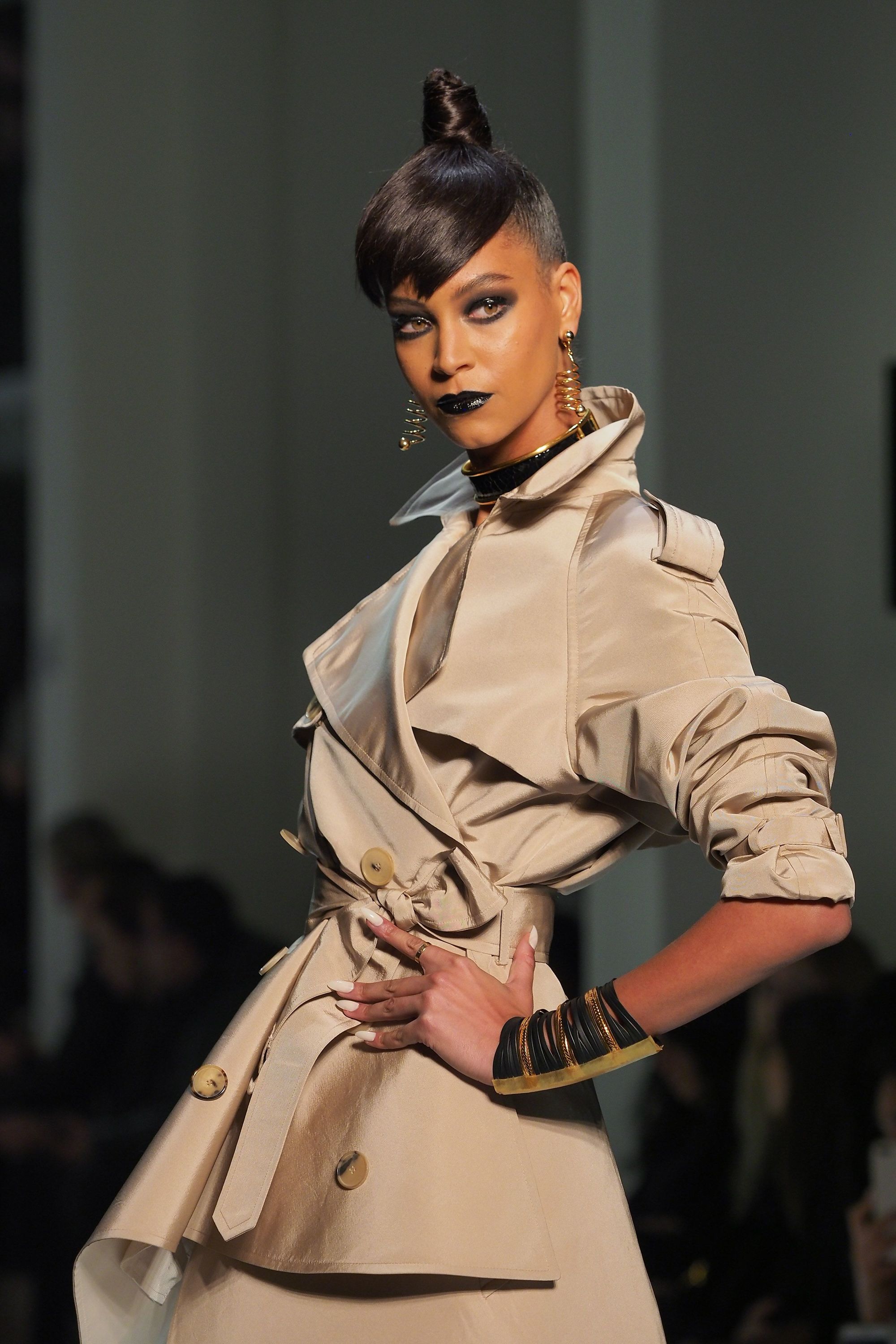 close up shot of model with high, sleek topknot with side part and undercut, wearing trench coat and posing on the jean paul gaultier paris haute couture ss18 runway