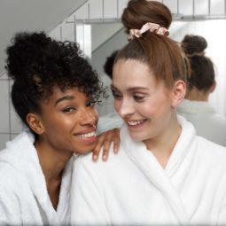 Leave-in conditioner: Shot of two girls in bathrobes, one with natural curly hair in a bun updo, the other with straight hair in a bun, too