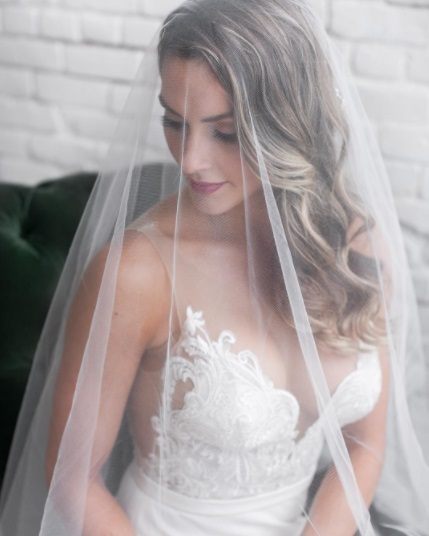 blonde bride with her hair in curls with a wedding veil covering her head