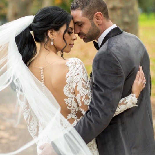 brunette bride with her hair in a ponytail standing with her husband