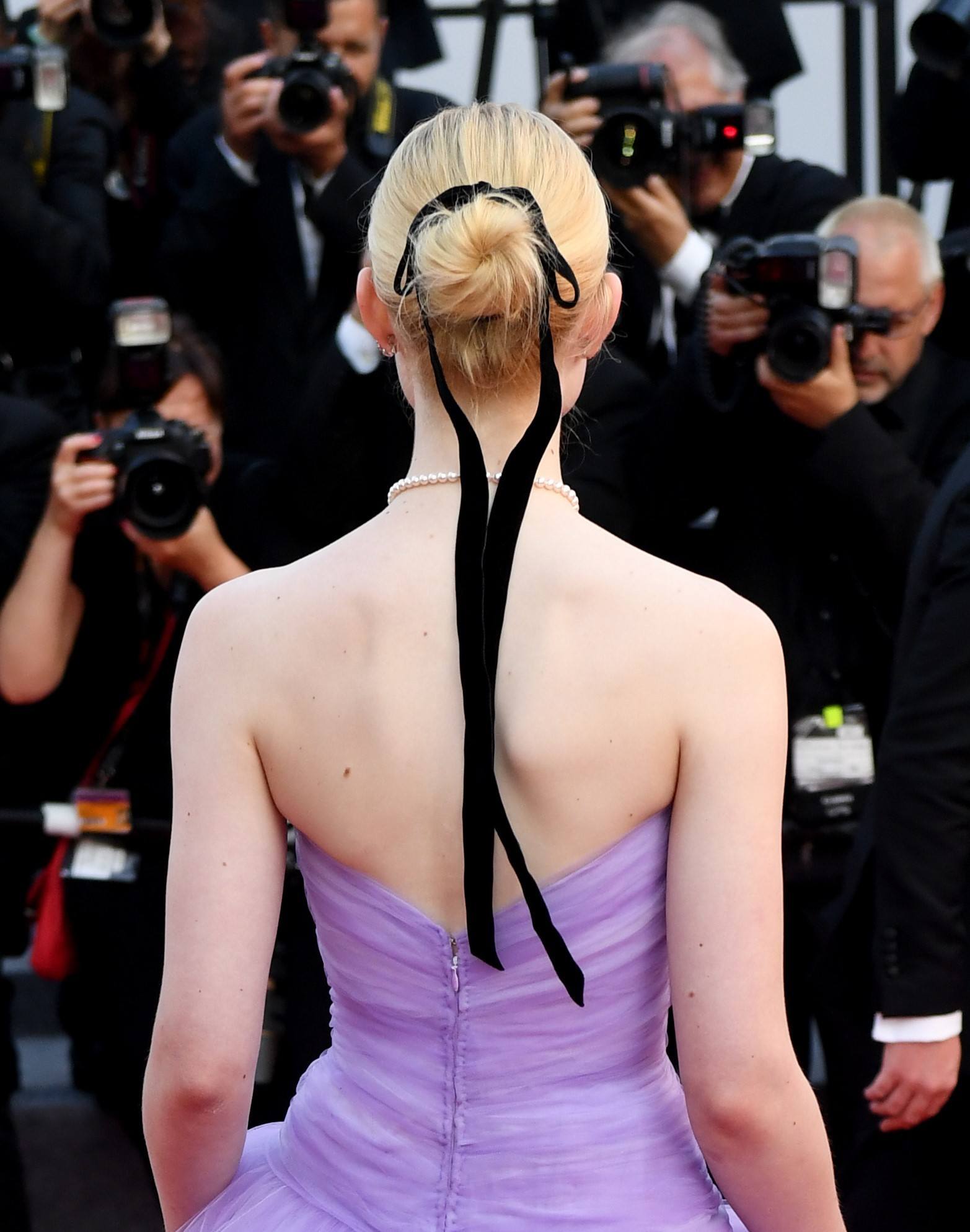 elle fanning on the red carpet with her blonde hair in a bun with a black ribbon wrapped around it
