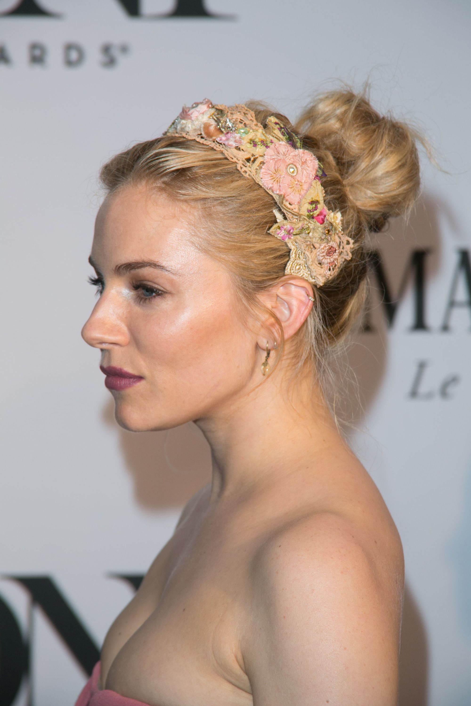 flower updo hairstyles: sienna miller with flower headband and messy bun updo on red carpet