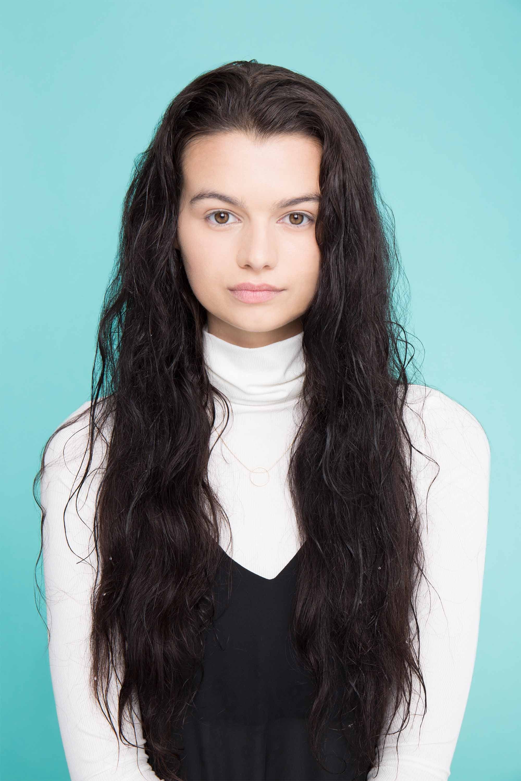 Shampoo full guide: Woman with long wavy dark brown hair wearing a long sleeve white top and black camisole.