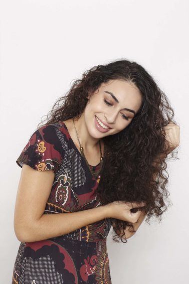 Model wtih long curly brown hair scrunching in hair product to the lengths wearing pattern top