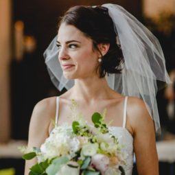 brunette bride with short bob length hair in a half up hairstyle wearing a lace veil and holding a bouquet