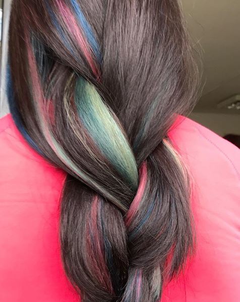 Close up of a woman with dark brown hair in a loose braid with streaks of green pink and blue hair colours