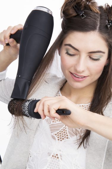 brunette woman using a round brush to blow dry her hair